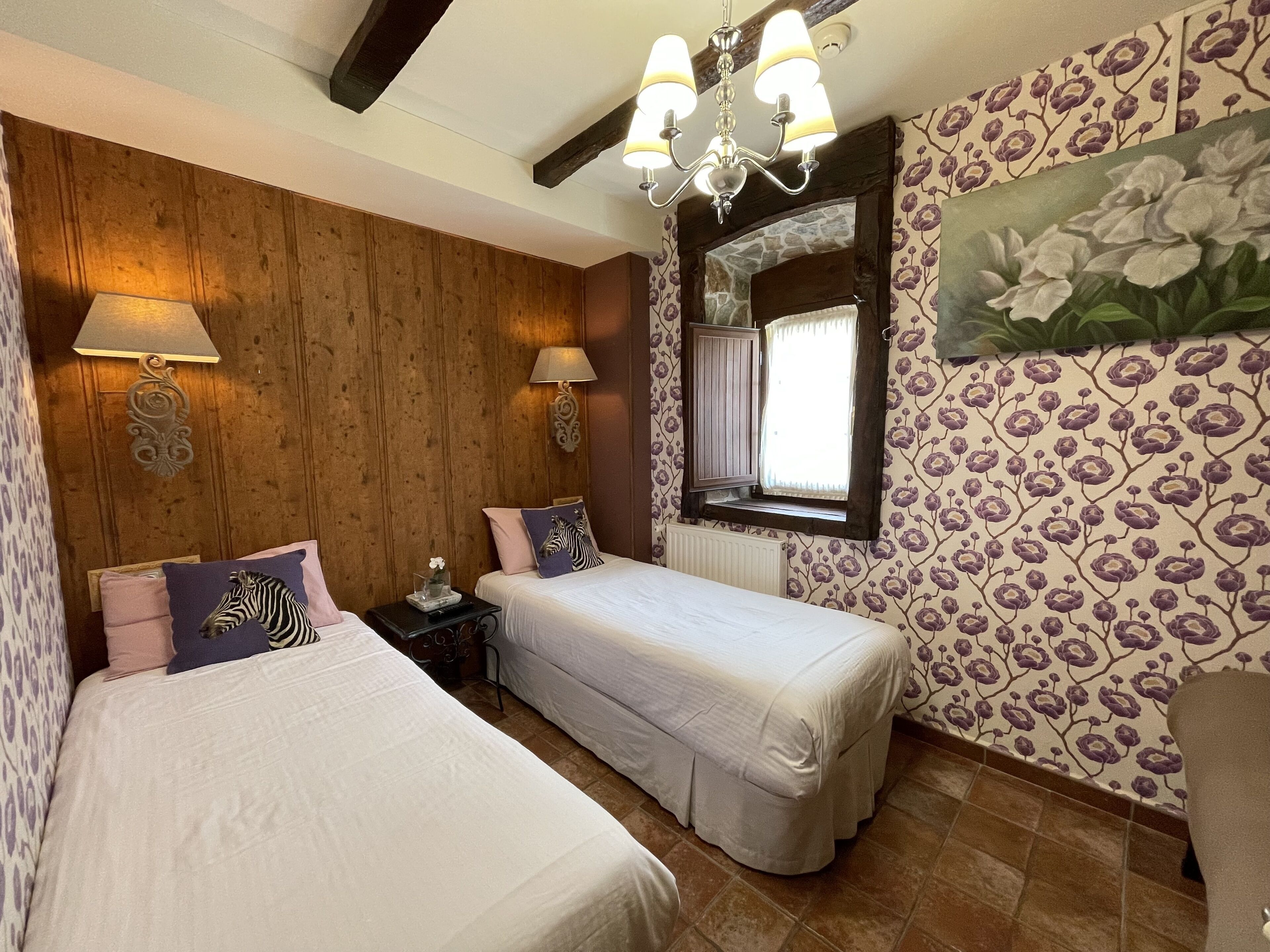 Une chambre avec deux lits, un lambris en bois, une fenêtre avec vue et un lustre.