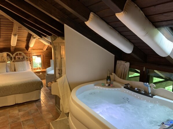 A bedroom with a large bed, a sitting area with a chair, and a hot tub.