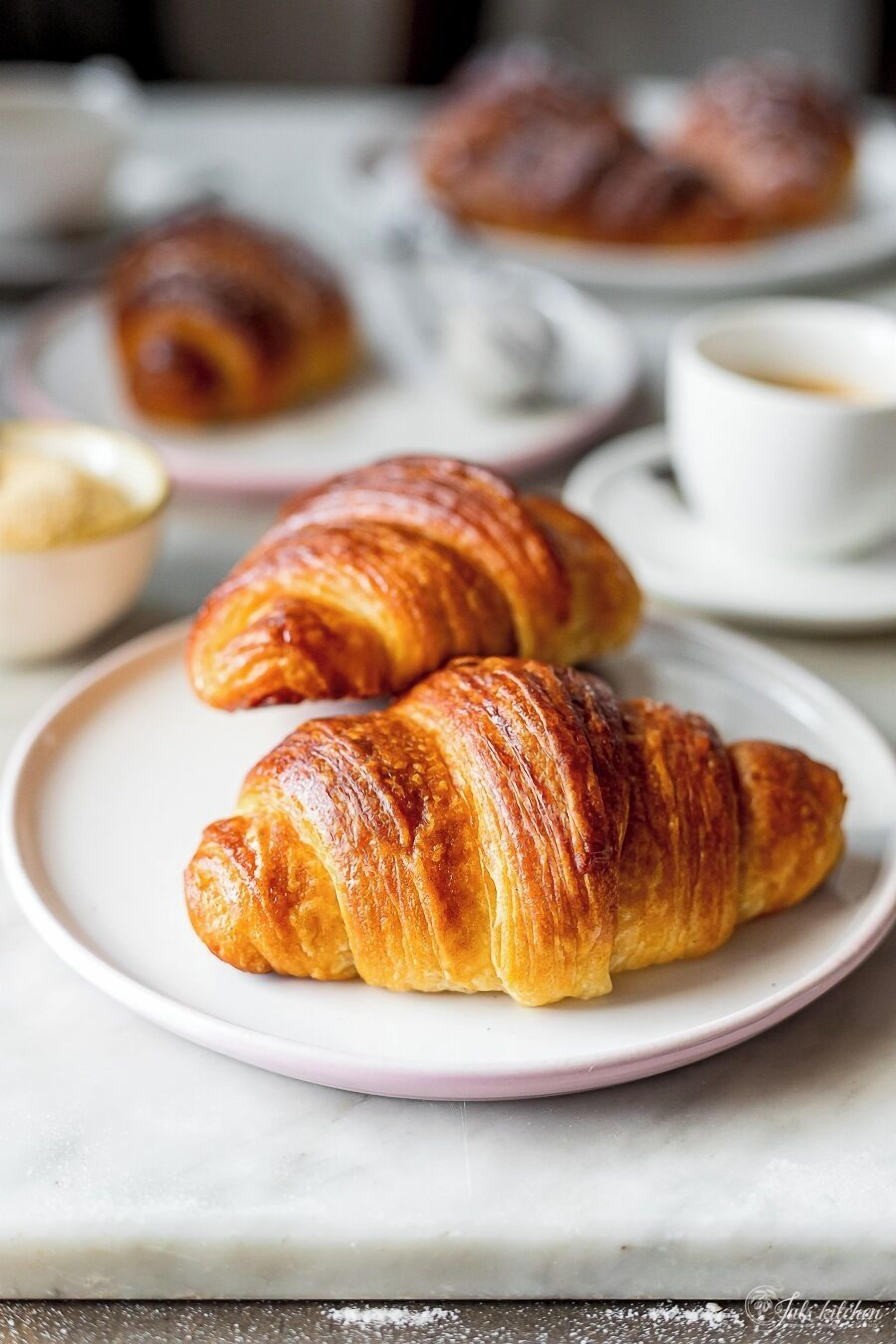 Two croissants on a plate with a cup of coffee in the background.