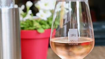 A glass of rosé wine with a label, a stainless steel container, and a red planter with white flowers.