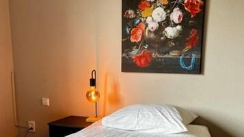 A hotel room with a neatly made bed, a painting of flowers on the wall, and a bedside lamp.