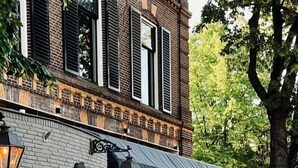 An outdoor seating area with wicker furniture and a brick wall with a lion mural. - Hotel de Roode Leeuw (Terborg)