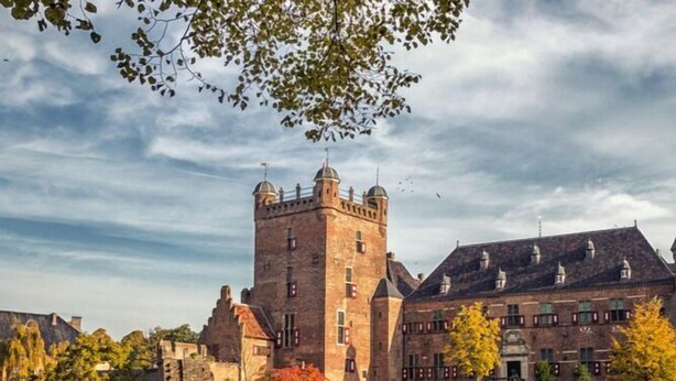 A historic castle with a moat, surrounded by well-maintained gardens and a calm body of water. - Hotel de Roode Leeuw (Terborg)