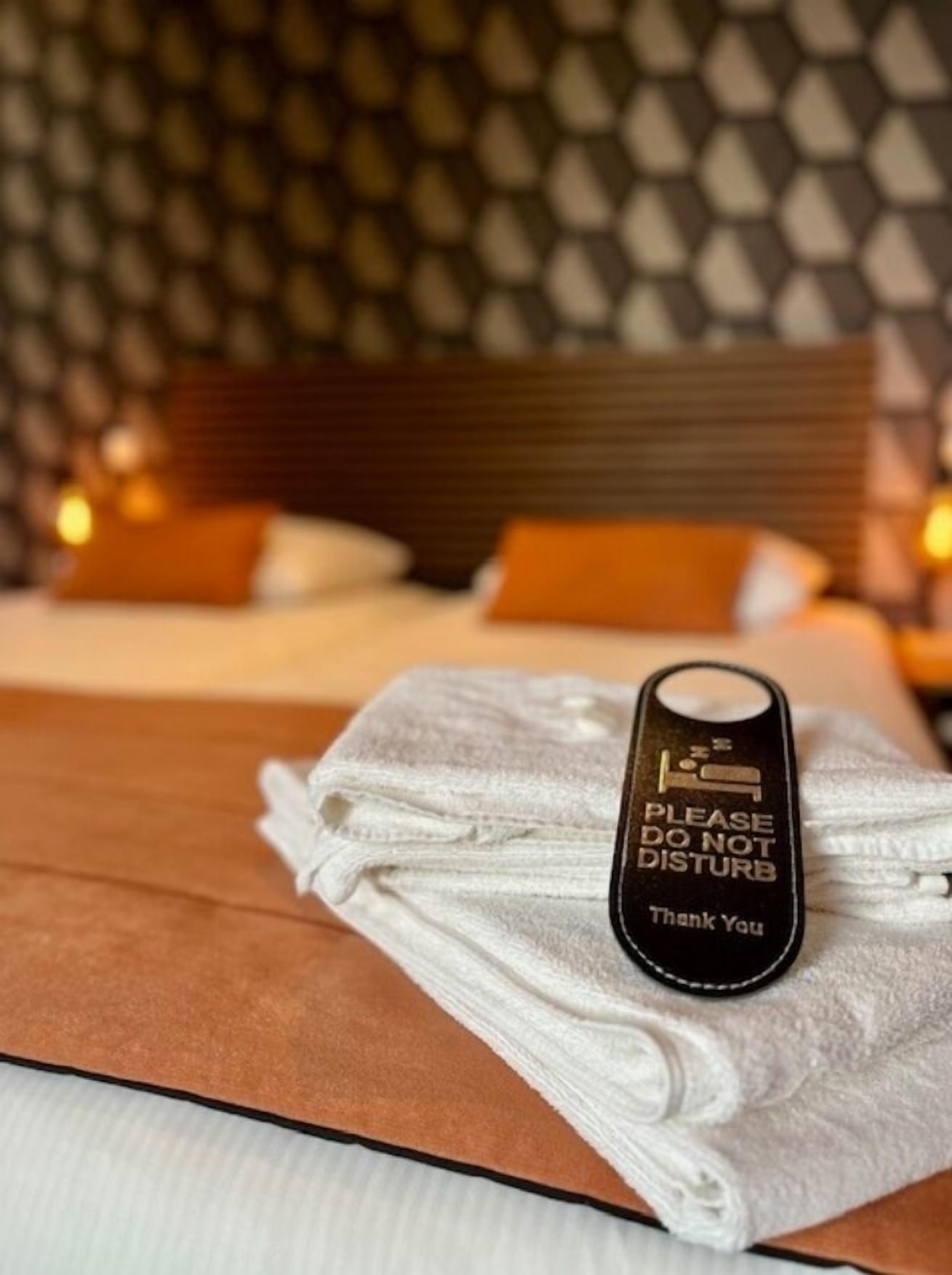 A neatly made bed with a folded towel and a black tag that reads "PLEASE DO NOT DISTURB Thank You".