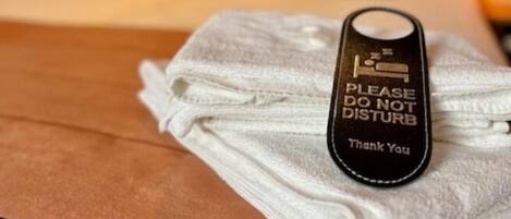 A neatly made bed with a folded towel and a black tag that reads "PLEASE DO NOT DISTURB Thank You".