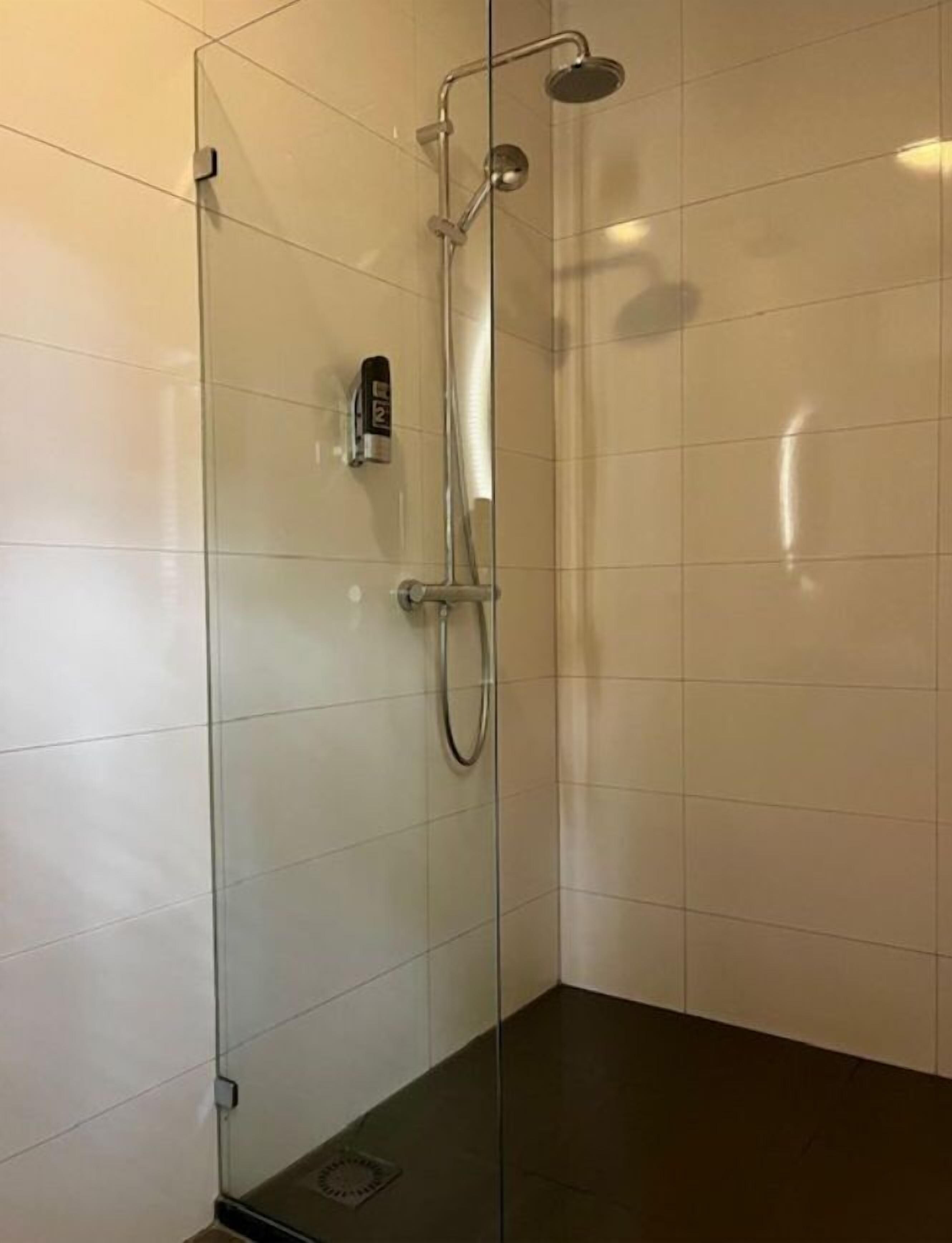 A glass-enclosed shower with a handheld showerhead and a wall-mounted faucet.