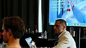 A conference room with a large screen displaying a presentation, a laptop, and two individuals seated. - Hotel de Roode Leeuw (Terborg)