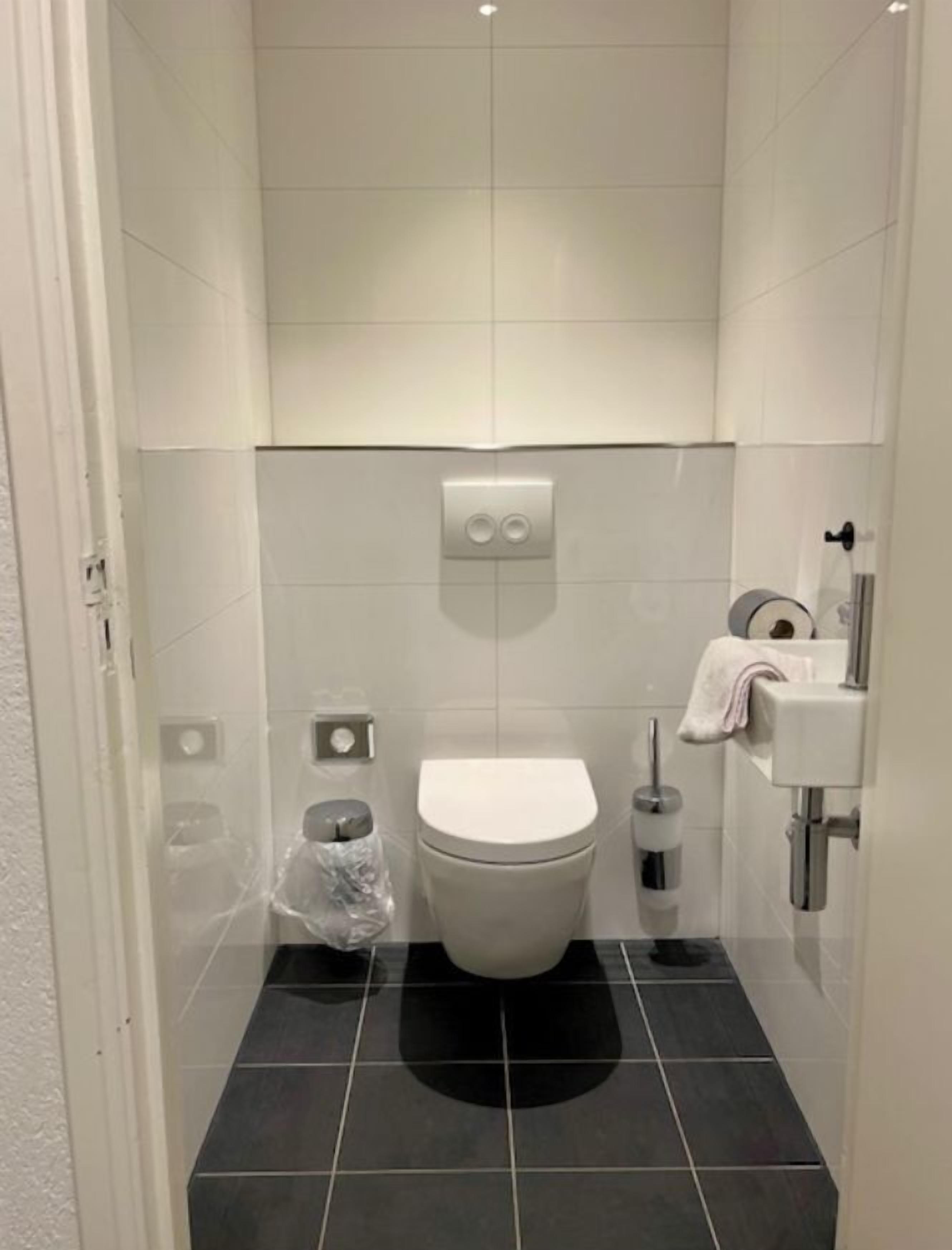 Un baño pequeño y moderno con inodoro, un cubo de basura, un porta papel higiénico y un lavabo.