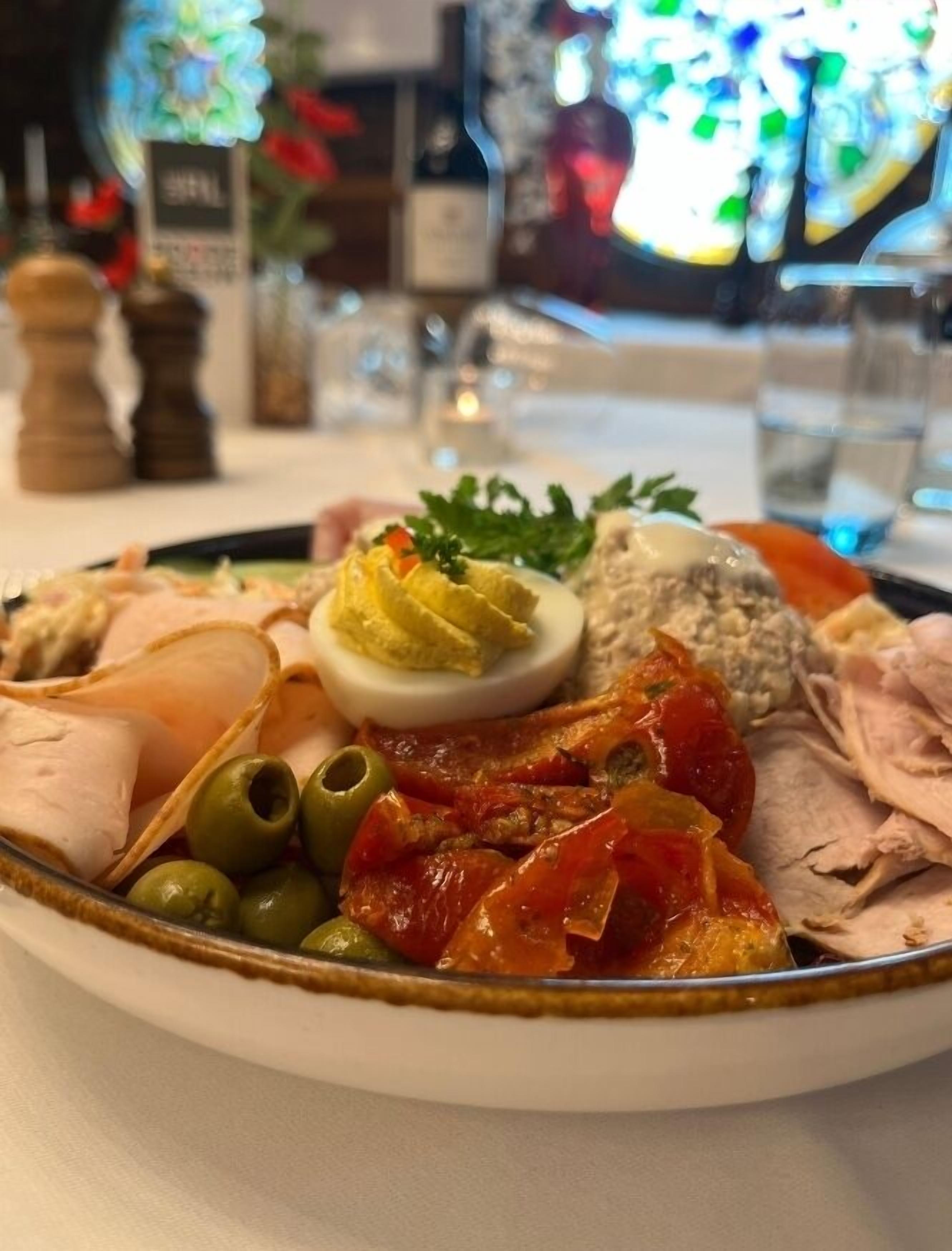 Um prato com diversos tipos de carne, azeitonas e um ovo cozido sobre uma mesa.