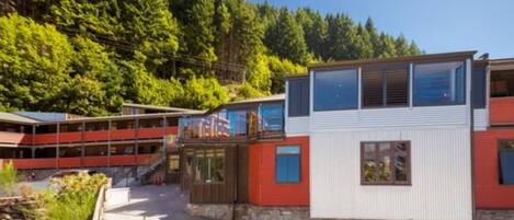 A modern building with a red and white facade, a covered walkway, and a view of a forested hillside.