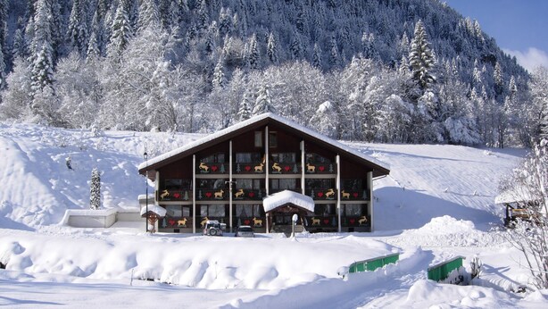A snow-covered lodge with a symmetrical facade, large windows, and a central entrance.