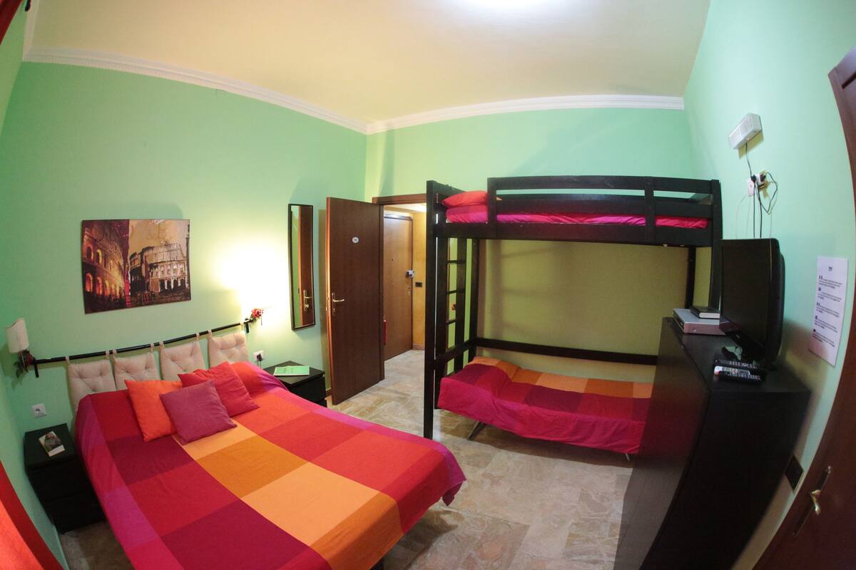 A room with a large bed, a bunk bed, a desk with a computer, and a television.