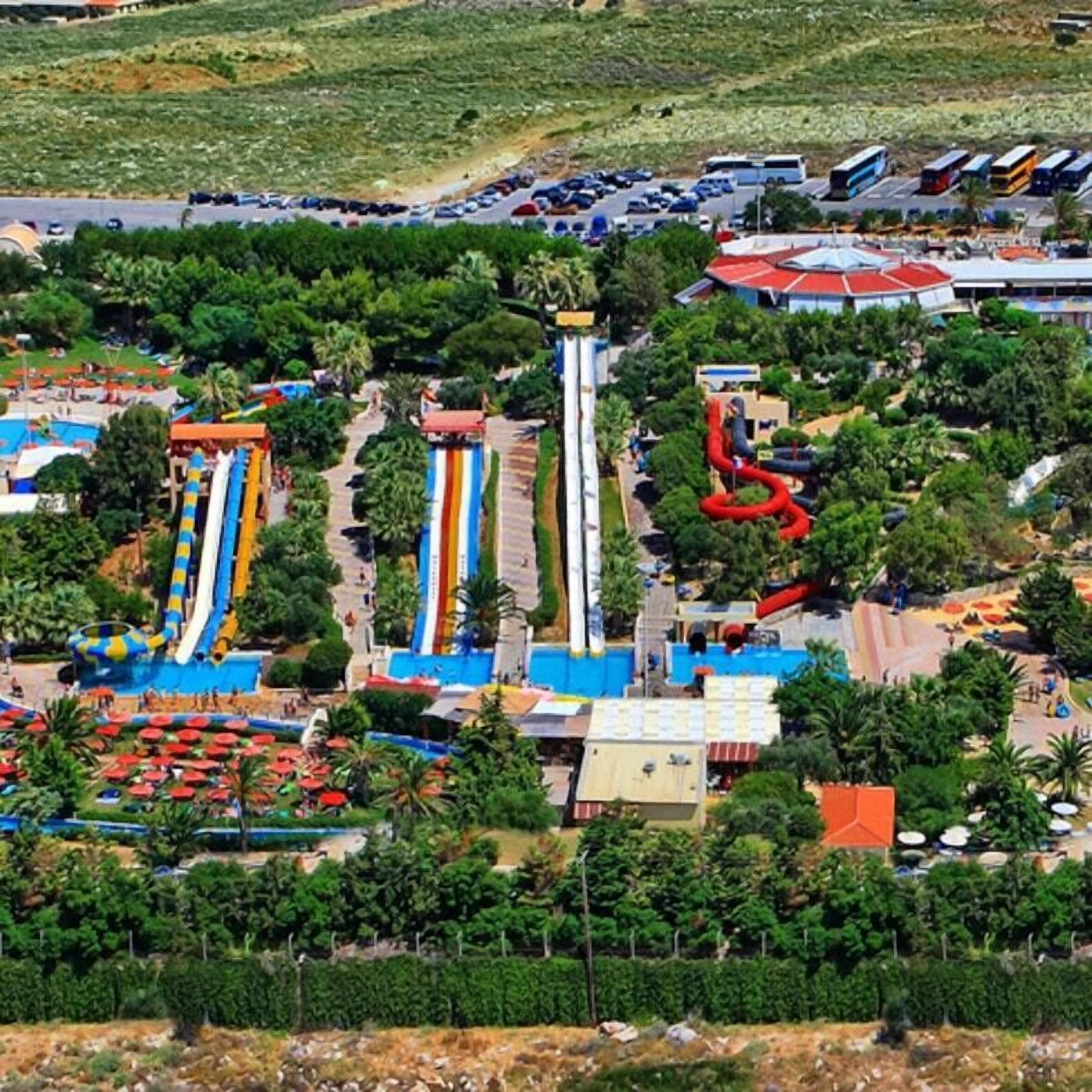 A water park with multiple slides and pools, surrounded by greenery and a parking area.