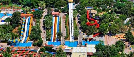 A water park with multiple slides and pools, surrounded by greenery and a parking area.