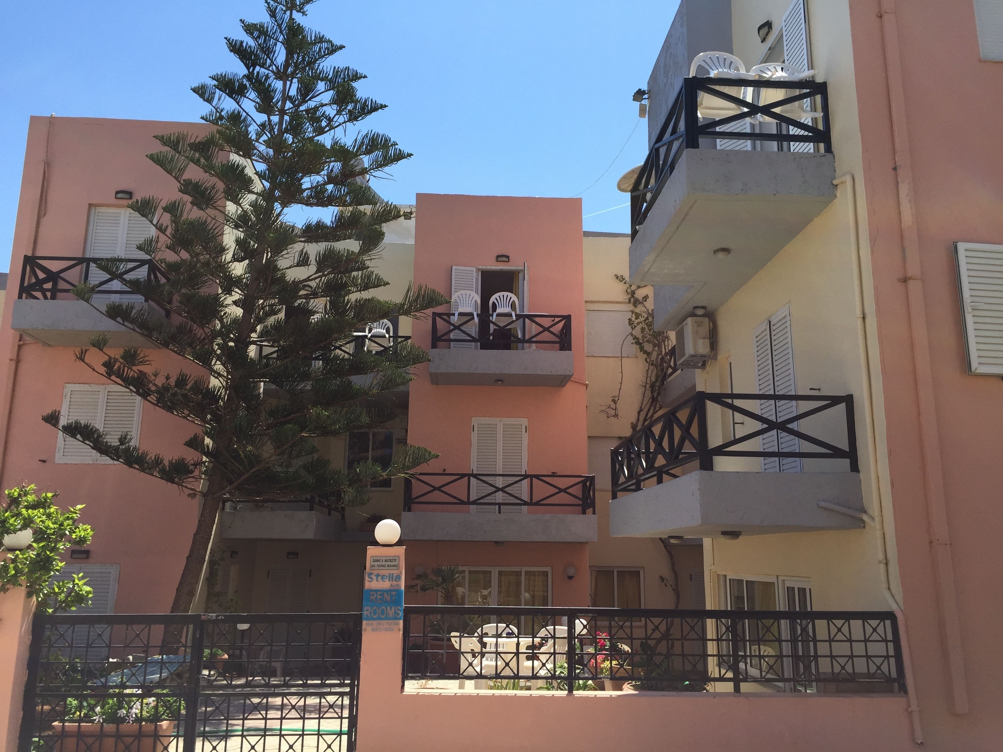 A multi-story building with balconies, a sign indicating rental rooms, and a tree in front.
