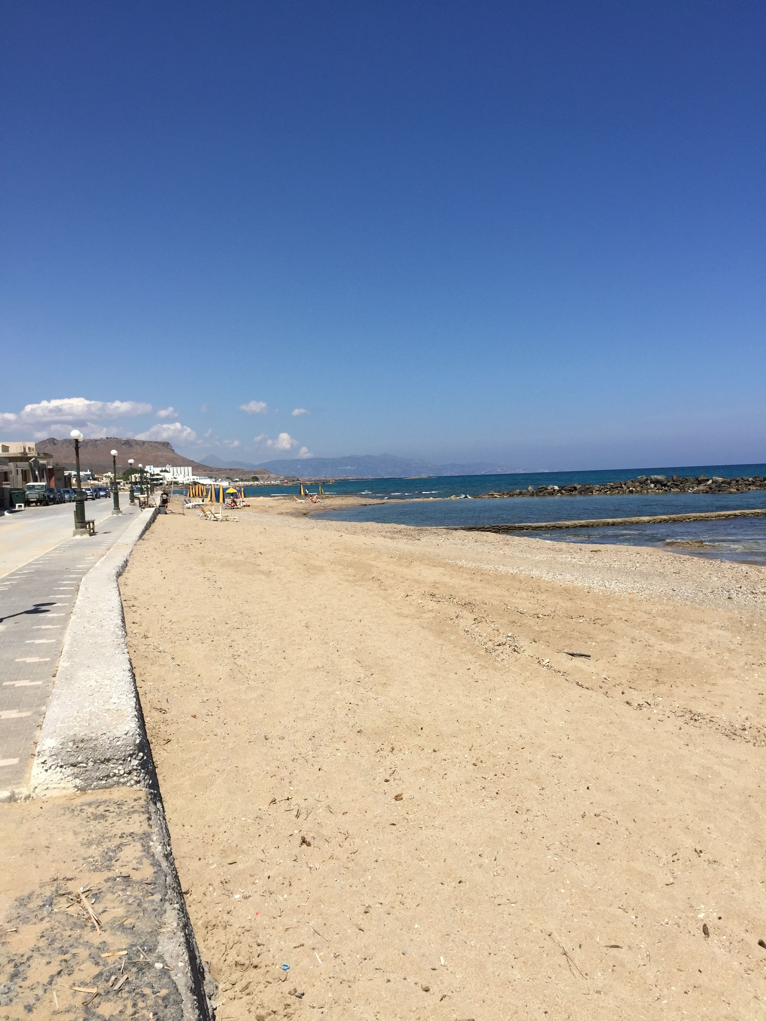 Una playa con un paseo adoquinado, sombrillas y una costa rocosa.