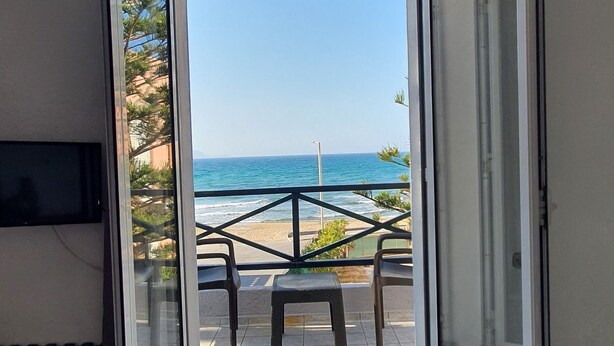 A room with a sliding glass door leading to a balcony with a view of the ocean. - Stella Apartments (Hersonissos)