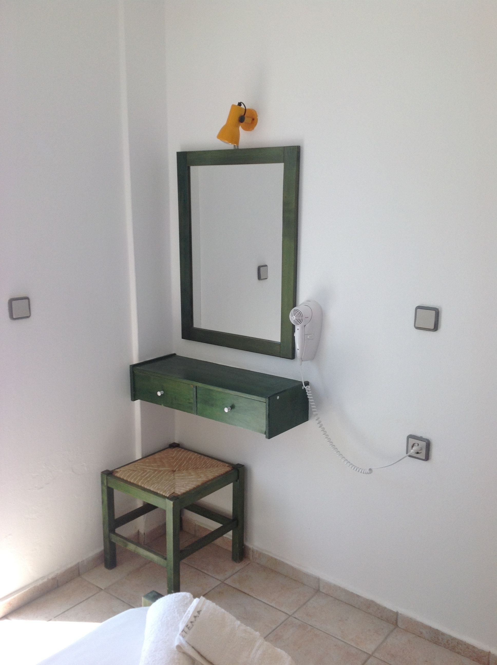 Un bagno piccolo con un mobile bagno verde, uno specchio, un asciugacapelli e una lampada gialla.