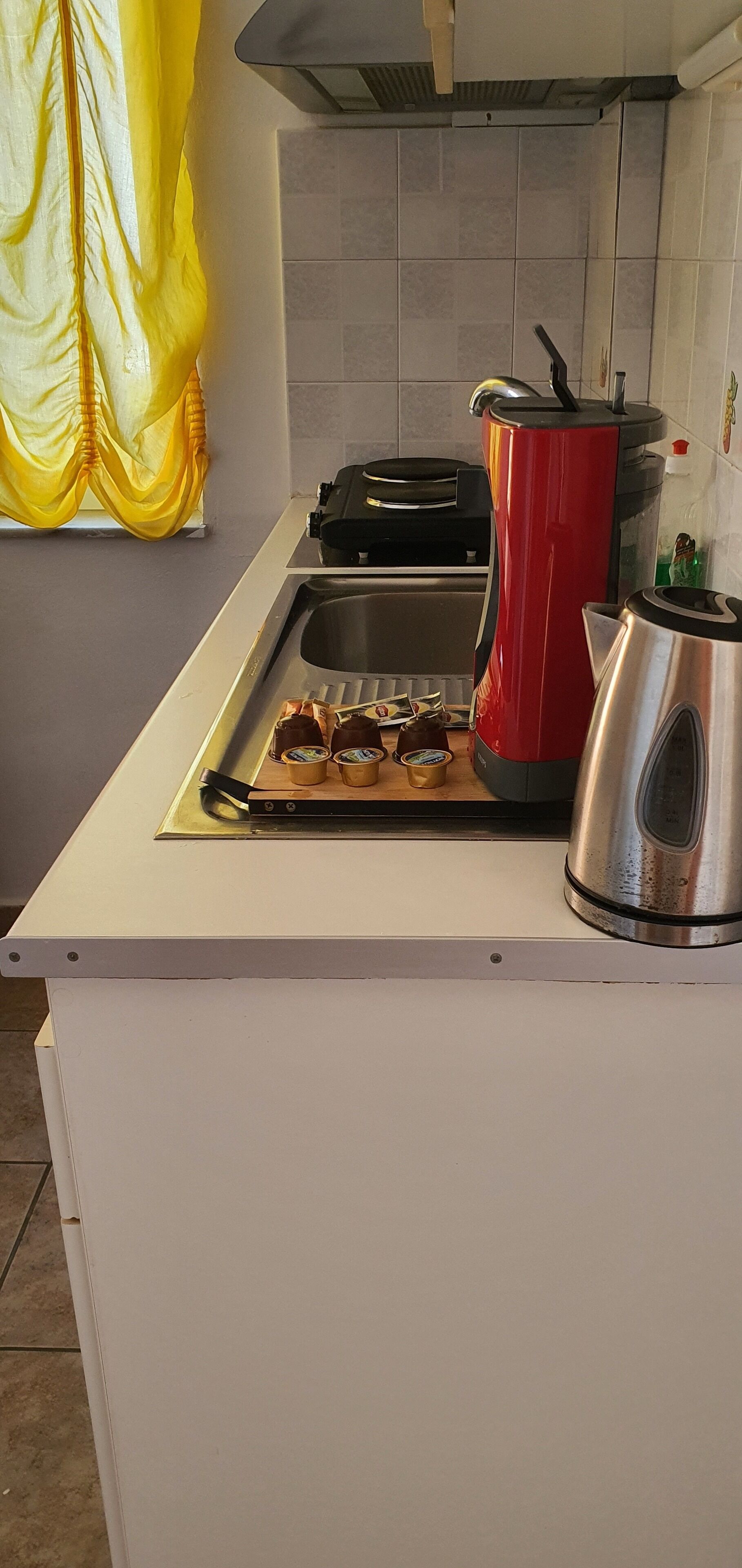 A kitchen with a stove, a red kettle, and a sink.