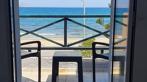 A view from a room with a glass door to a balcony overlooking a beach with a railing and a bench. - Stella Apartments (Hersonissos)