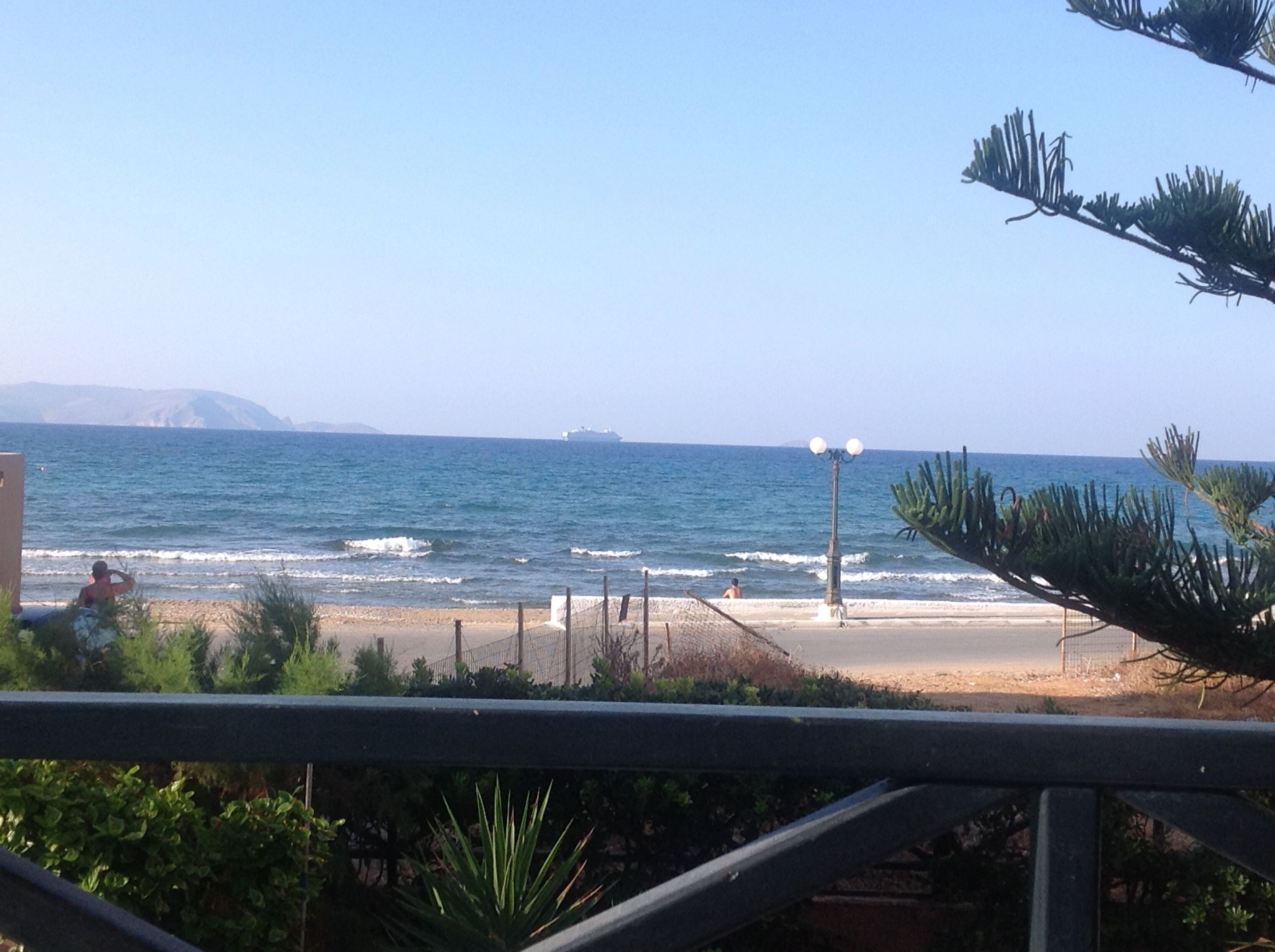 Vista de la playa con olas, un barco a lo lejos y cielo despejado.