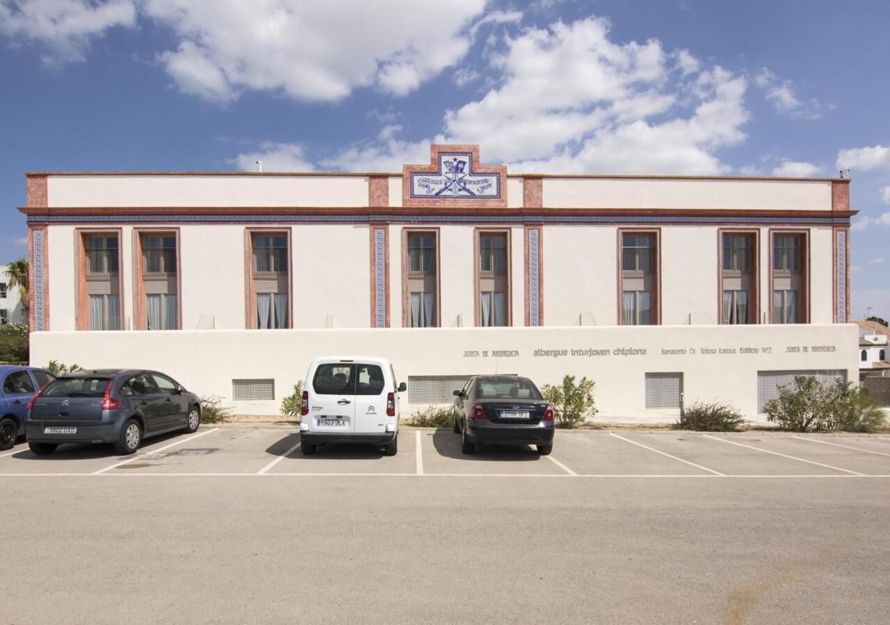 A building with a white facade, multiple windows, and a parking lot with three cars.