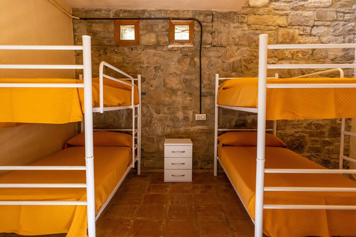 Un dormitorio con literas dobles, un pequeño aparador blanco y una pared de piedra.