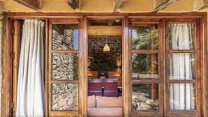 Una habitación con paredes de piedra, vigas de madera y chimenea de piedra. Hay dos sillas y una mesa frente a la chimenea.