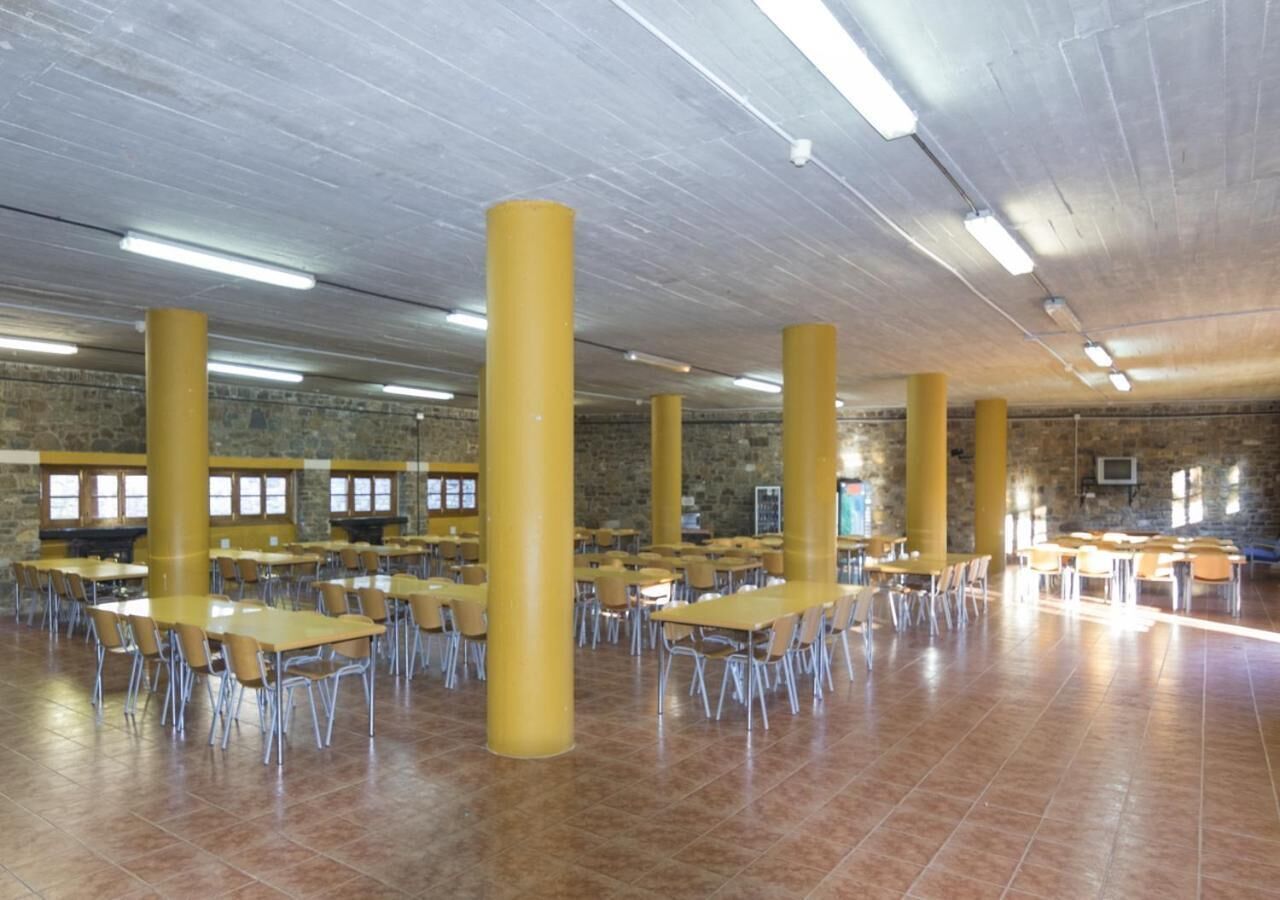 A spacious indoor area with yellow pillars, tiled flooring, and multiple tables and chairs arranged for dining.