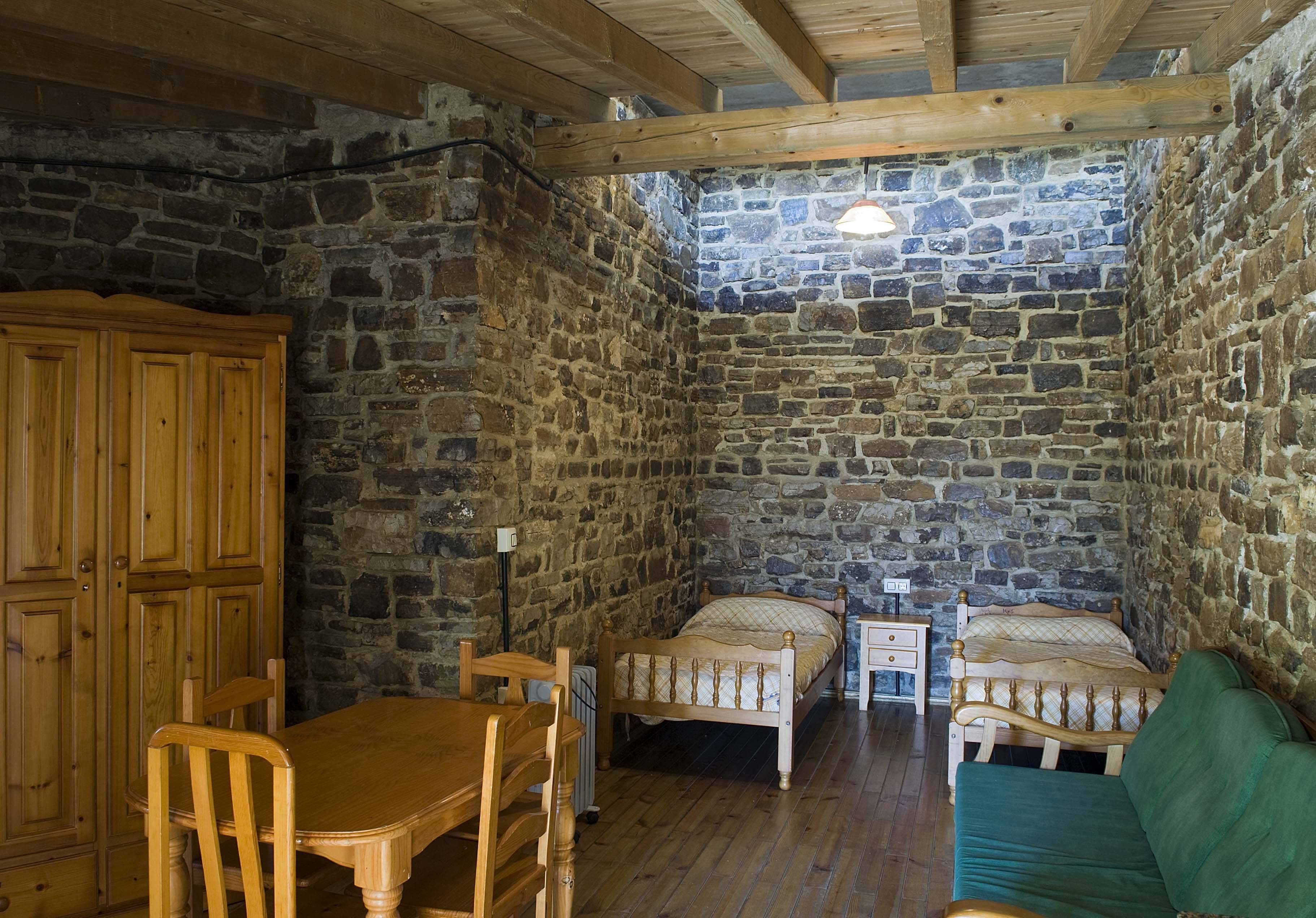 Une pièce rustique aux murs de pierre, avec un lit en bois, une table en bois et un canapé vert.