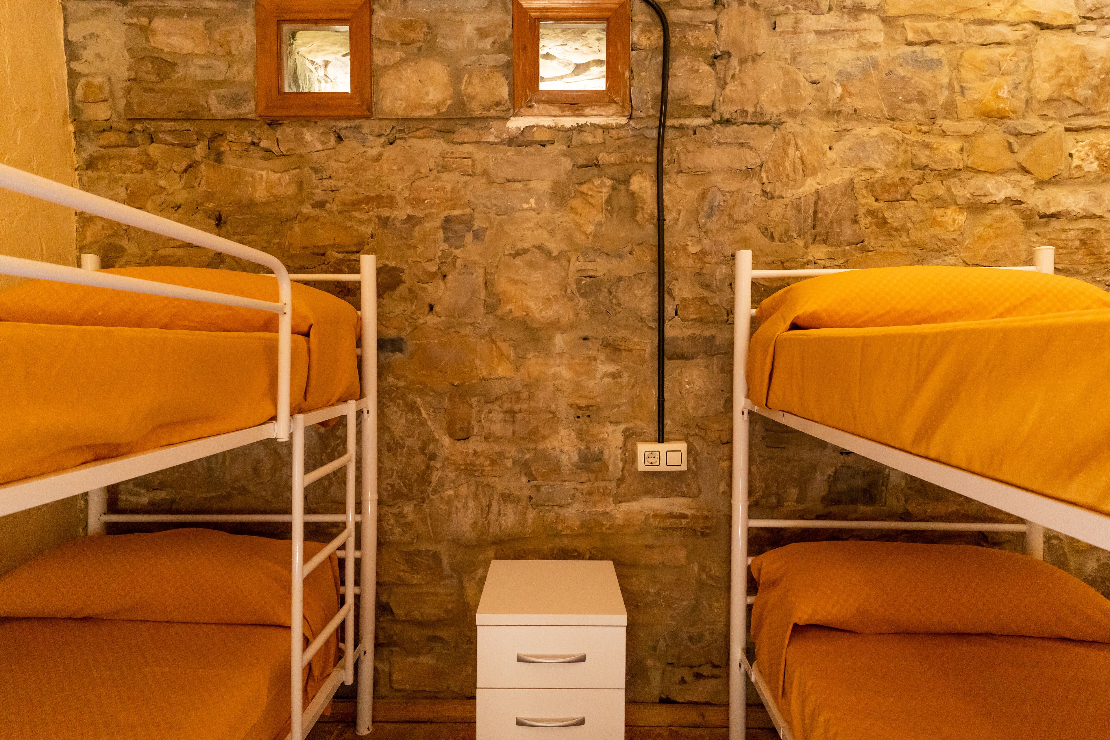 Dormitori amb lliteres, parets de pedra i una petita finestra.