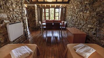 Una habitación rústica con paredes de piedra, piso de madera, una mesa de comedor con sillas y dos camas con toallas.