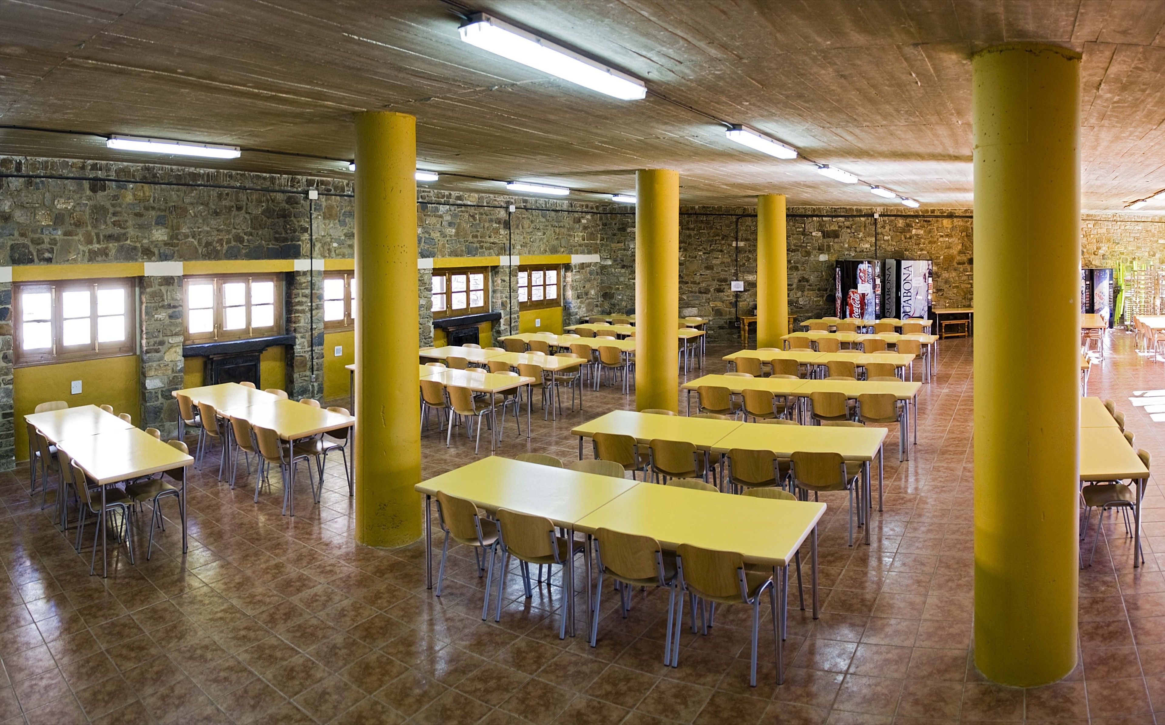 A spacious room with multiple yellow tables and chairs, stone walls, and a tiled floor.