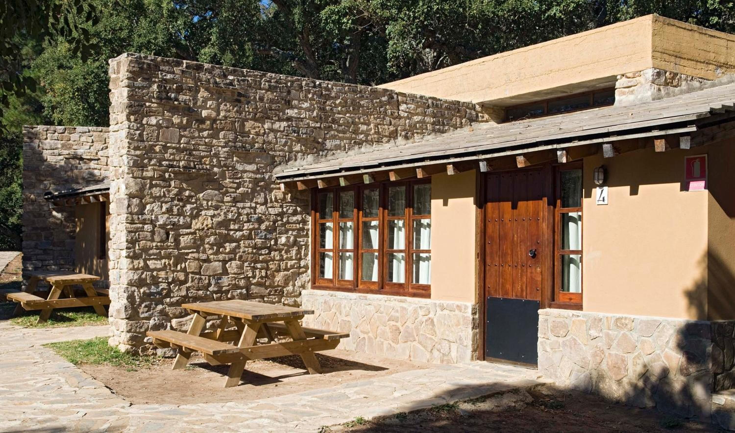 A stone building with a wooden door and windows, a picnic table, and a stone wall.