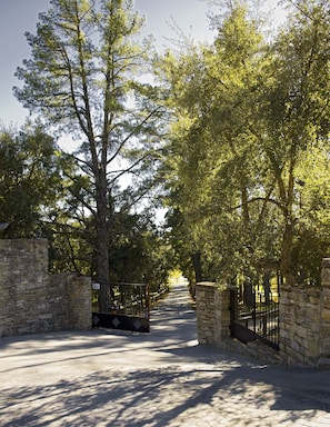 A paved pathway flanked by stone walls and metal gates, leading through a tree-lined area.