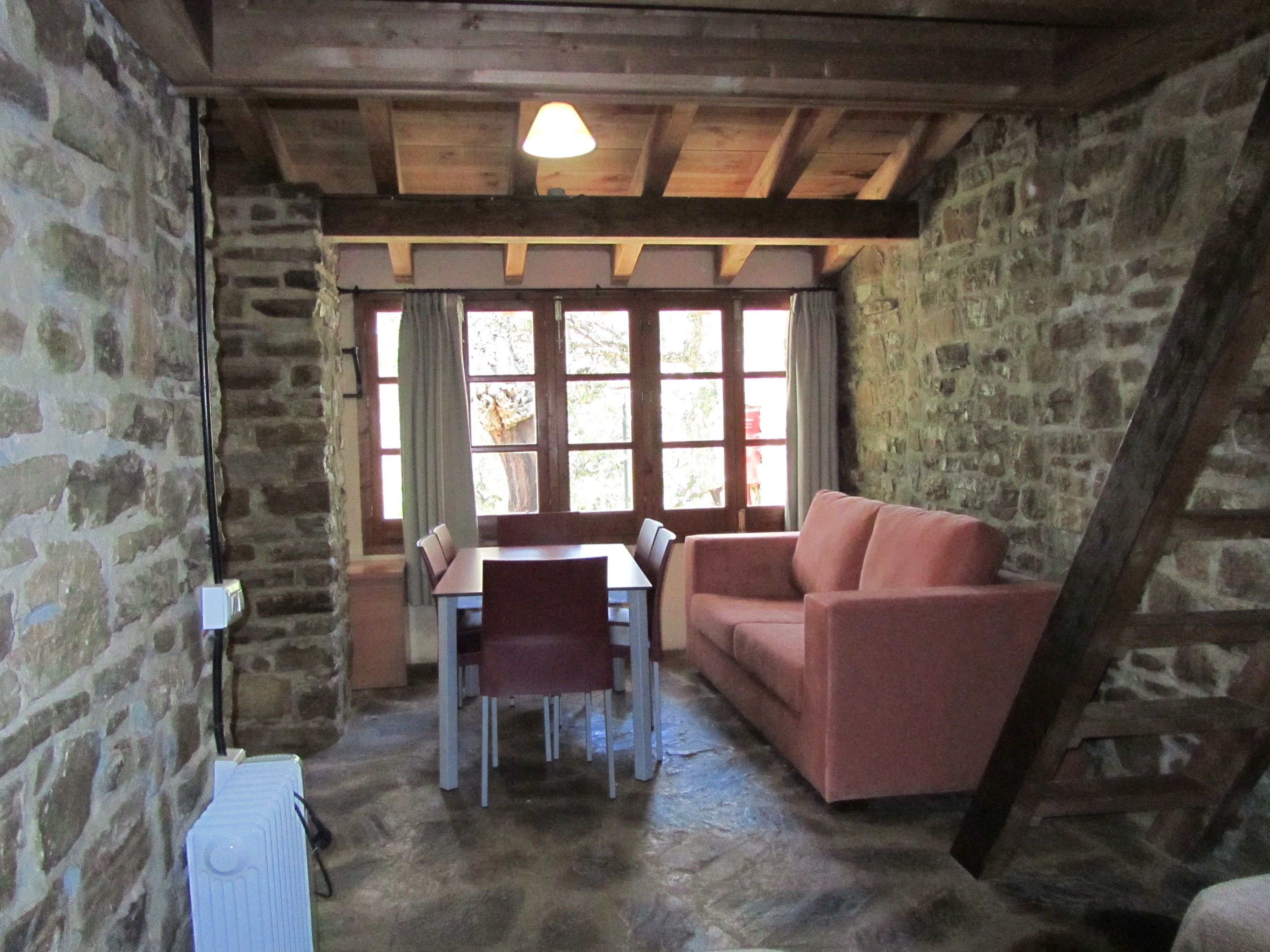 Una habitación rústica con paredes de piedra, techo de madera, una mesa de comedor con sillas, un sofá y un radiador.