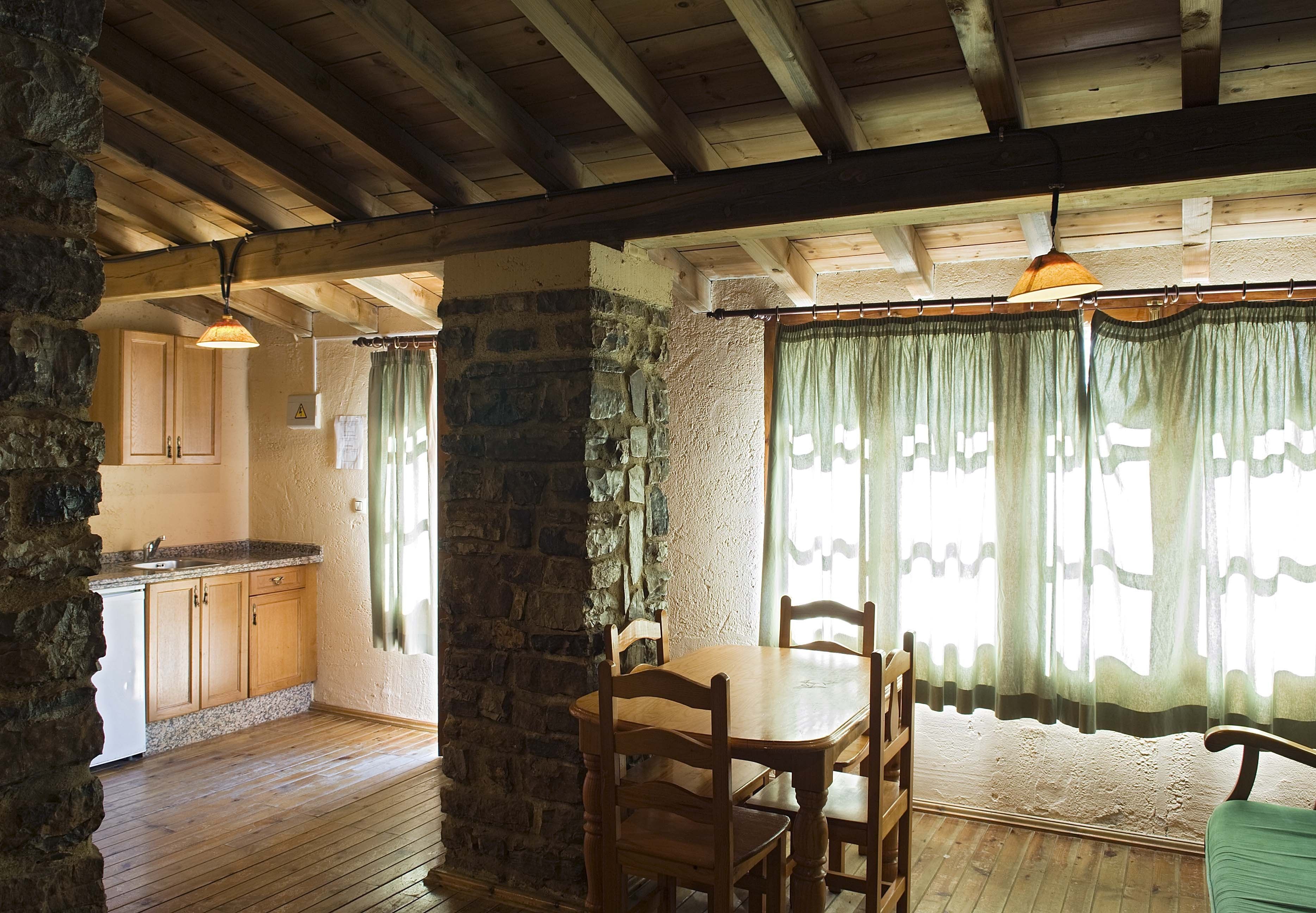 A rustic kitchen with wooden cabinets, a stone wall, and a dining area with a wooden table and chairs.