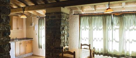 A rustic kitchen with wooden cabinets, a stone wall, and a dining area with a wooden table and chairs.