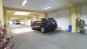 A parking garage with multiple cars, fluorescent lighting, and a potted plant. - Hotel Alexander (Trujillo)