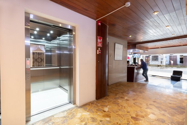 An elevator with a glass door, a reception desk, and a stone-tiled floor.