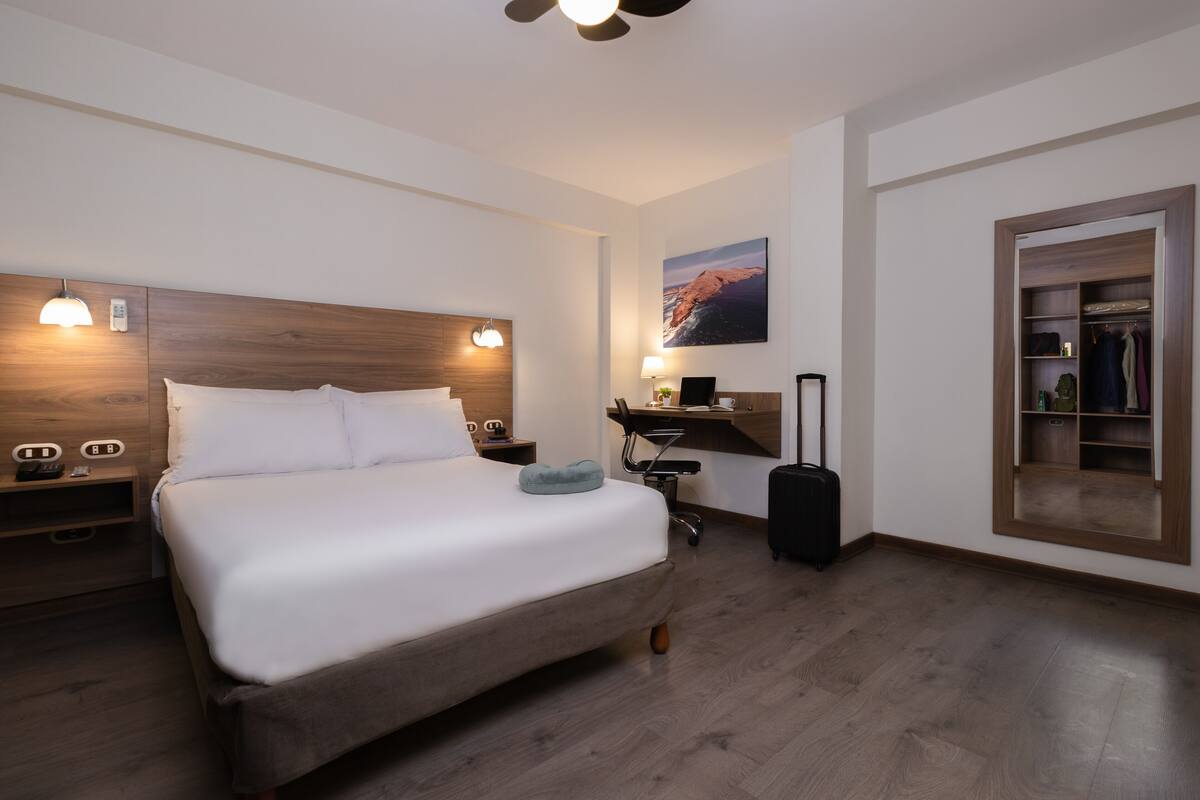 Una habitación de hotel con una cama grande, un escritorio, una silla, una maleta y un armario.