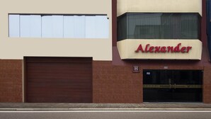 A hotel named 'Alexander' with a beige facade, multiple windows, and a brown garage door. - Hotel Alexander (Trujillo)