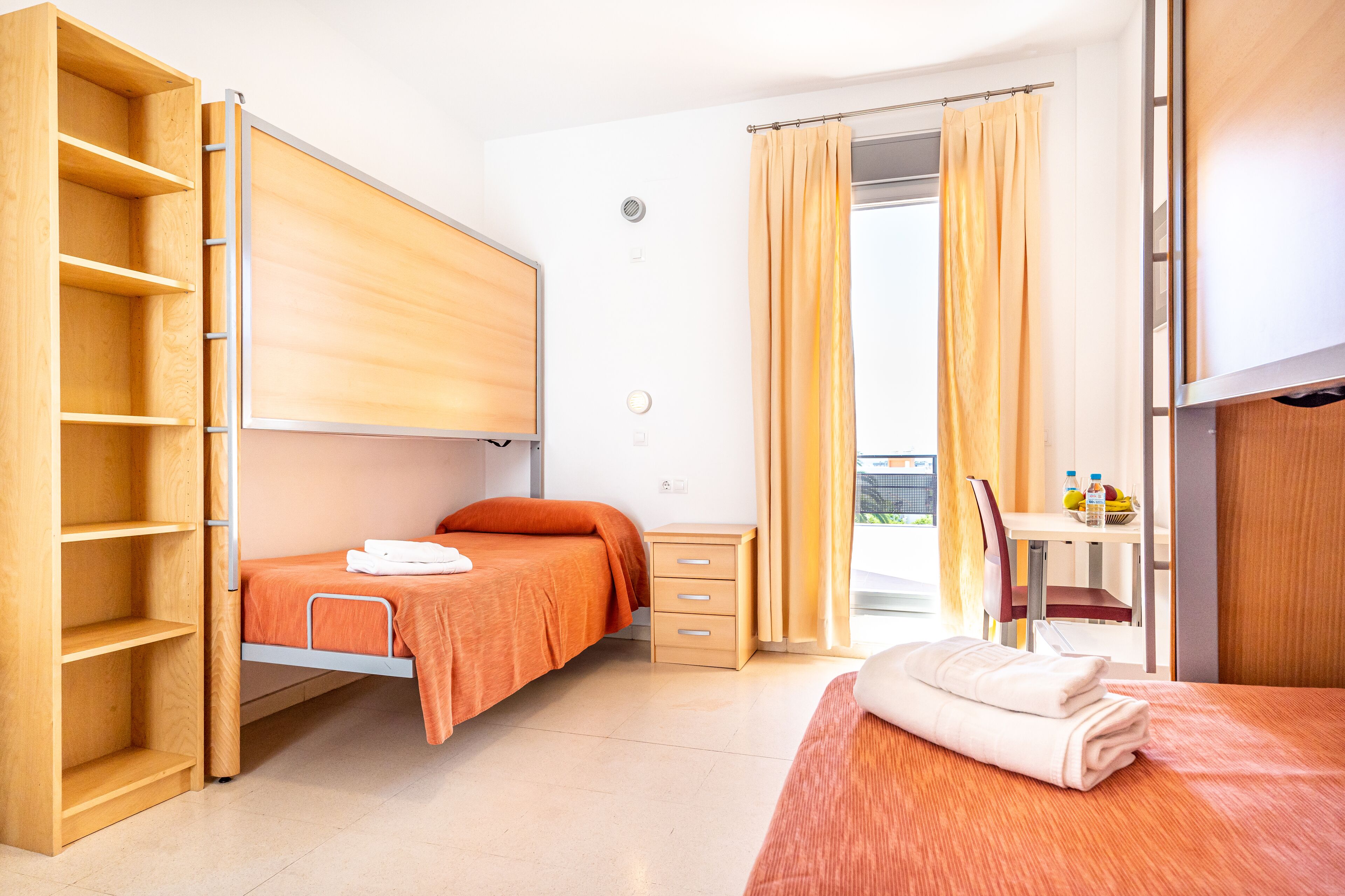 Een hotelkamer met een stapelbed, een bureau met een stoel en een raam met gordijnen.