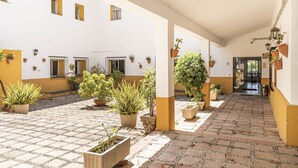 Un patio con plantas en macetas, piso de baldosas y un edificio de paredes amarillas y blancas.