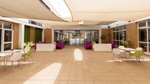 An outdoor patio area with modern seating arrangements, including white and green chairs and purple sofas, under a large canopy. - Albergue Inturjoven Sevilla - Hostel (Seville)