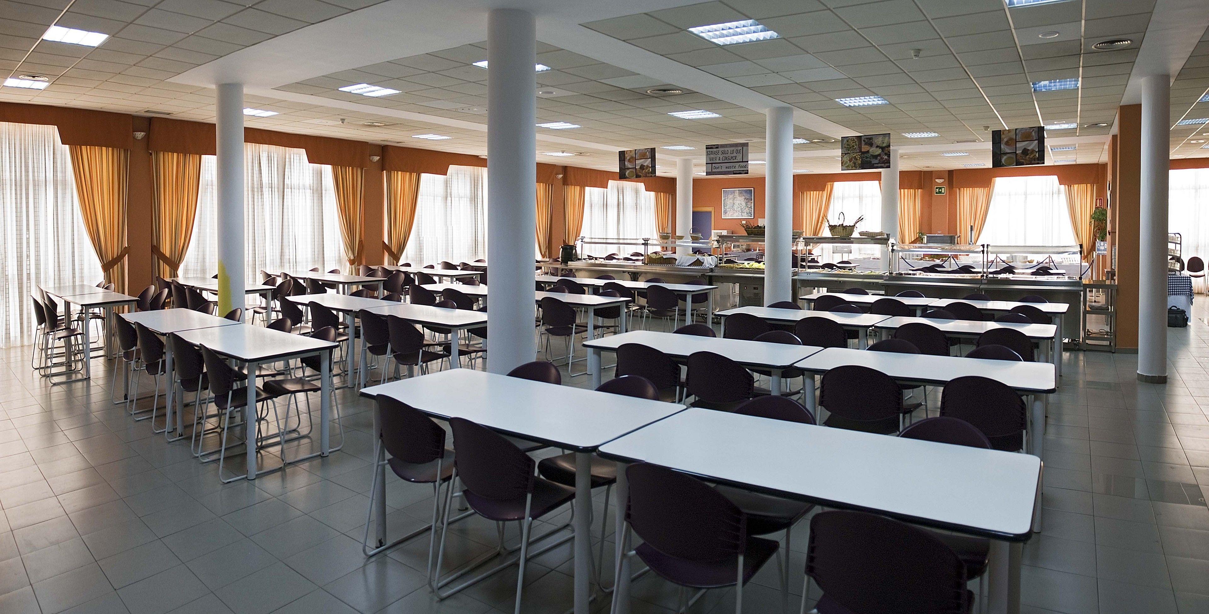 Un comedor amplio con varias mesas y sillas, ventanas grandes con cortinas y un diseño moderno y elegante.
