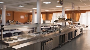 A buffet setup with multiple serving stations, a large central serving area, and a seating area with tables and chairs. - Albergue Inturjoven Sevilla - Hostel (Seville)