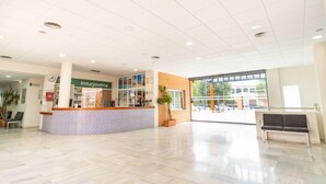 A spacious lobby with a reception desk, a large window, and a bench. - Albergue Inturjoven Sevilla - Hostel (Seville)