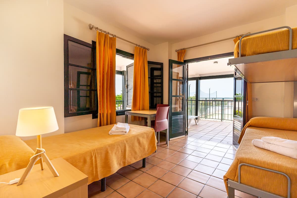 A hotel room with a bed, a desk with a lamp, a chair, and a balcony with a view.