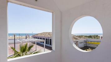 Una habitación con un amplio ventanal que da a una playa y un edificio de fachada blanca.
